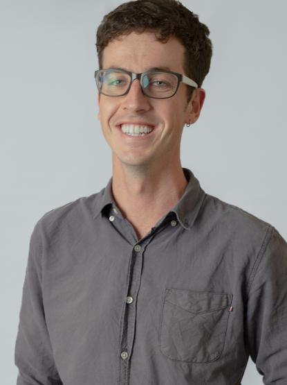 A picture of a person with short brown hair wearing glasses and a grey button up shirt