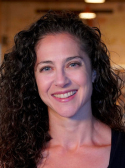 A person with dark curly hair smiling at the camera