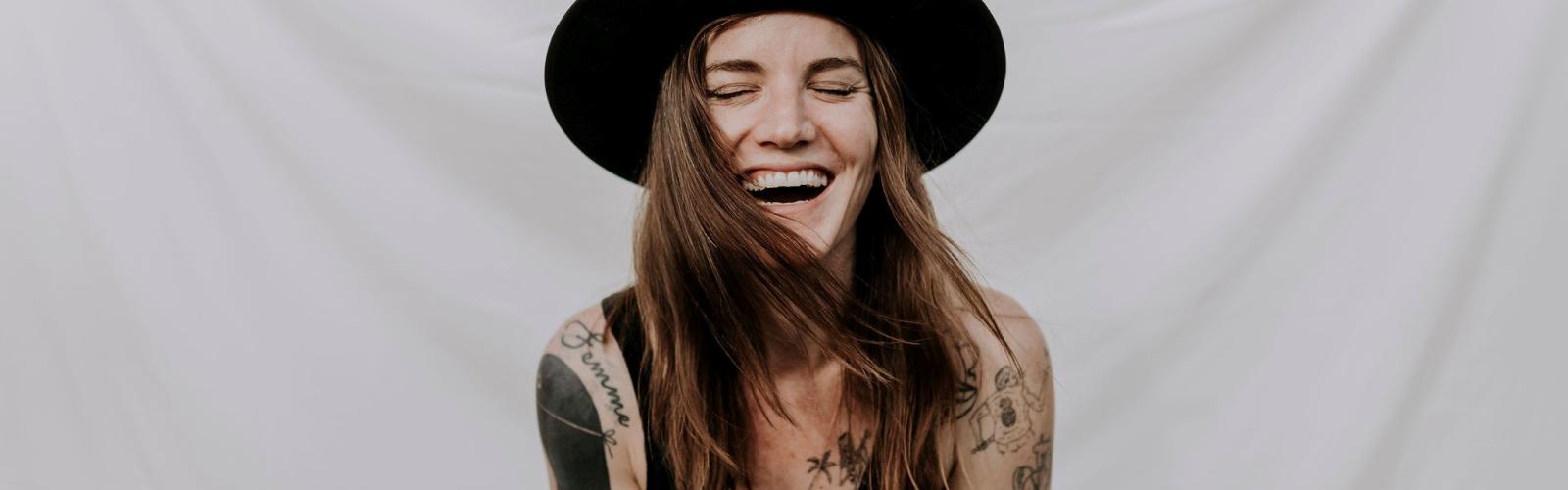 Image of Abbe May singer, smilling wearing a black hat and tank top with tattoos on her arms
