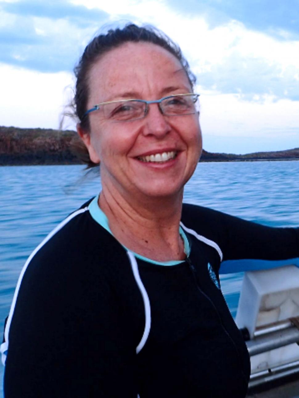 A lady in a wetsuit on a boat, smiling.