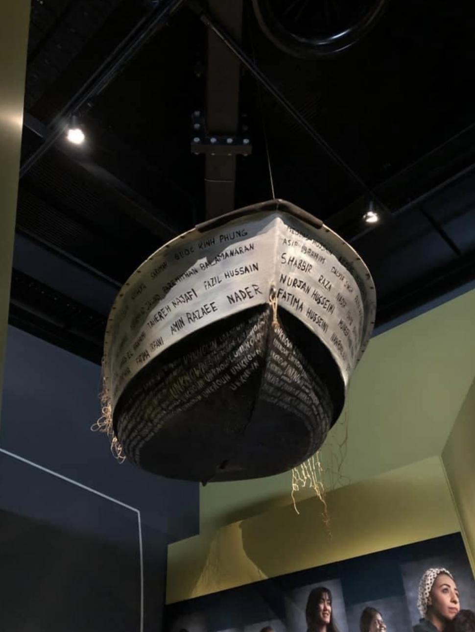 A suspended artwork in the shape of a boat with names written all along the sides