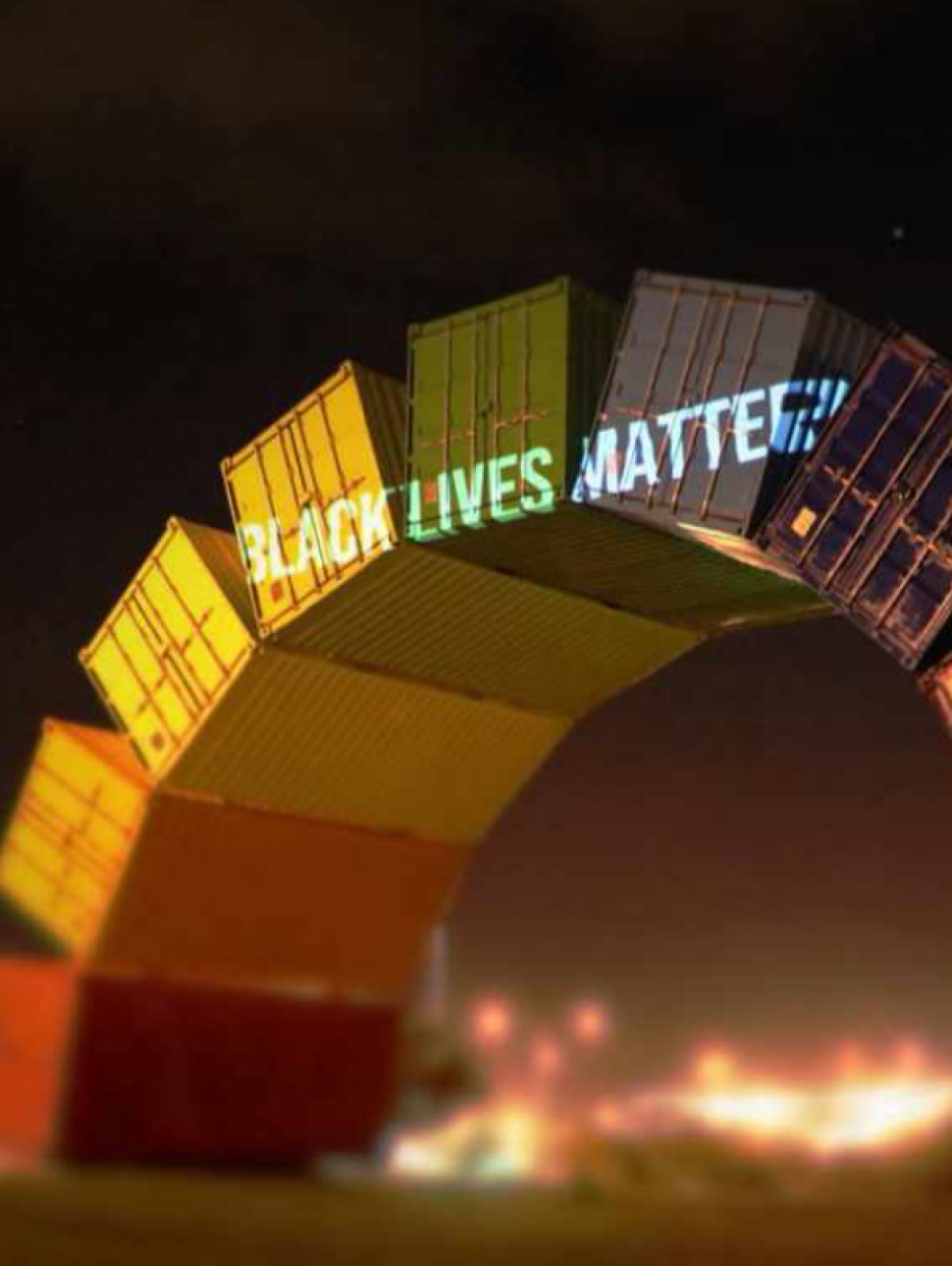 A rainbow of painted shipping containers with 'Black Lives Matter' projected at the top of the arc