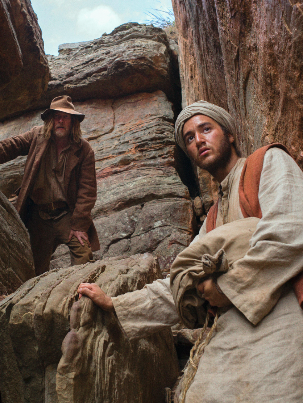 Two people stand in a rocky crevice, looking seriously towards the camera