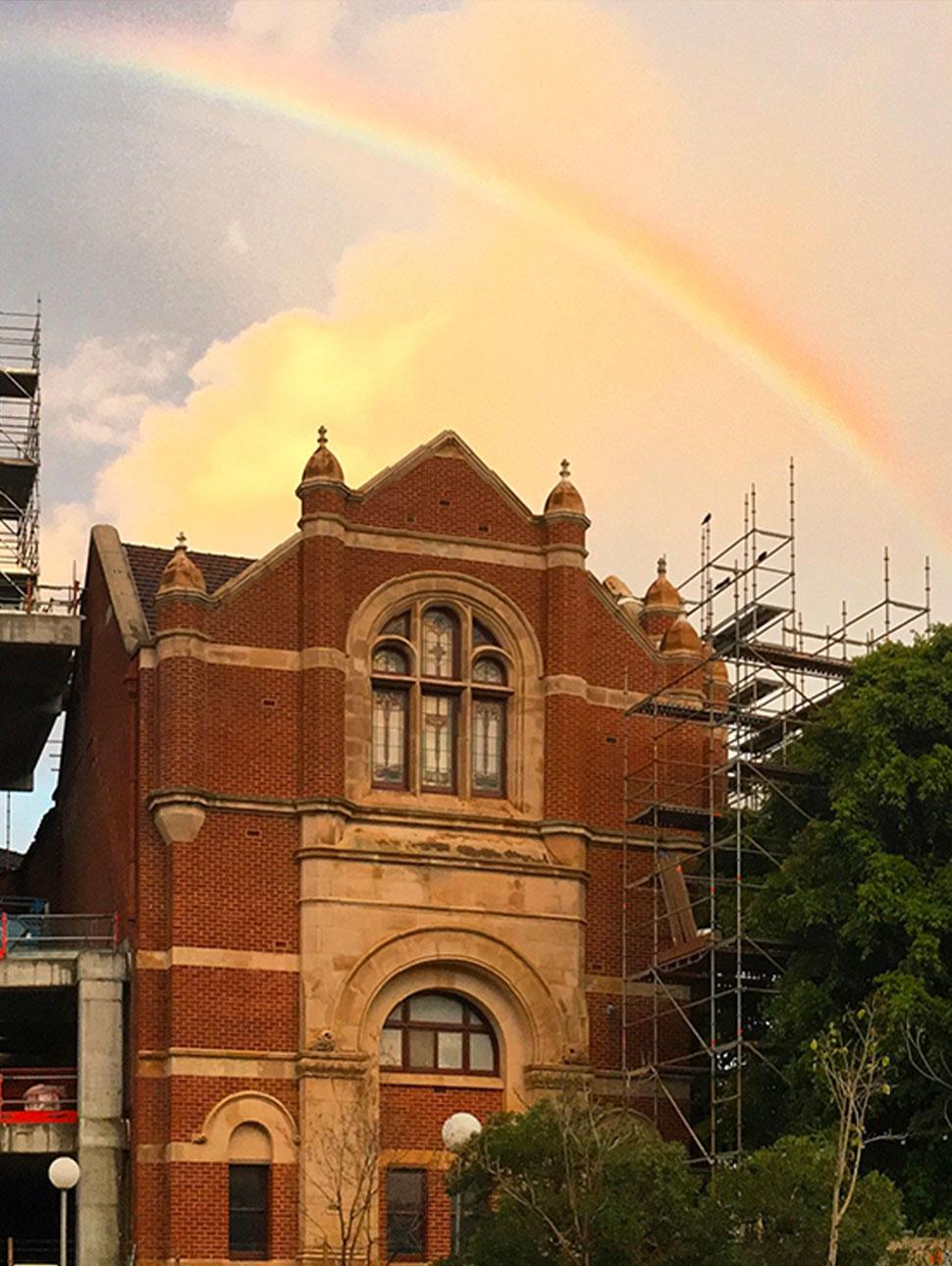 A rainbow glows in the sky above a heritage building which is surrounded by scaffolding