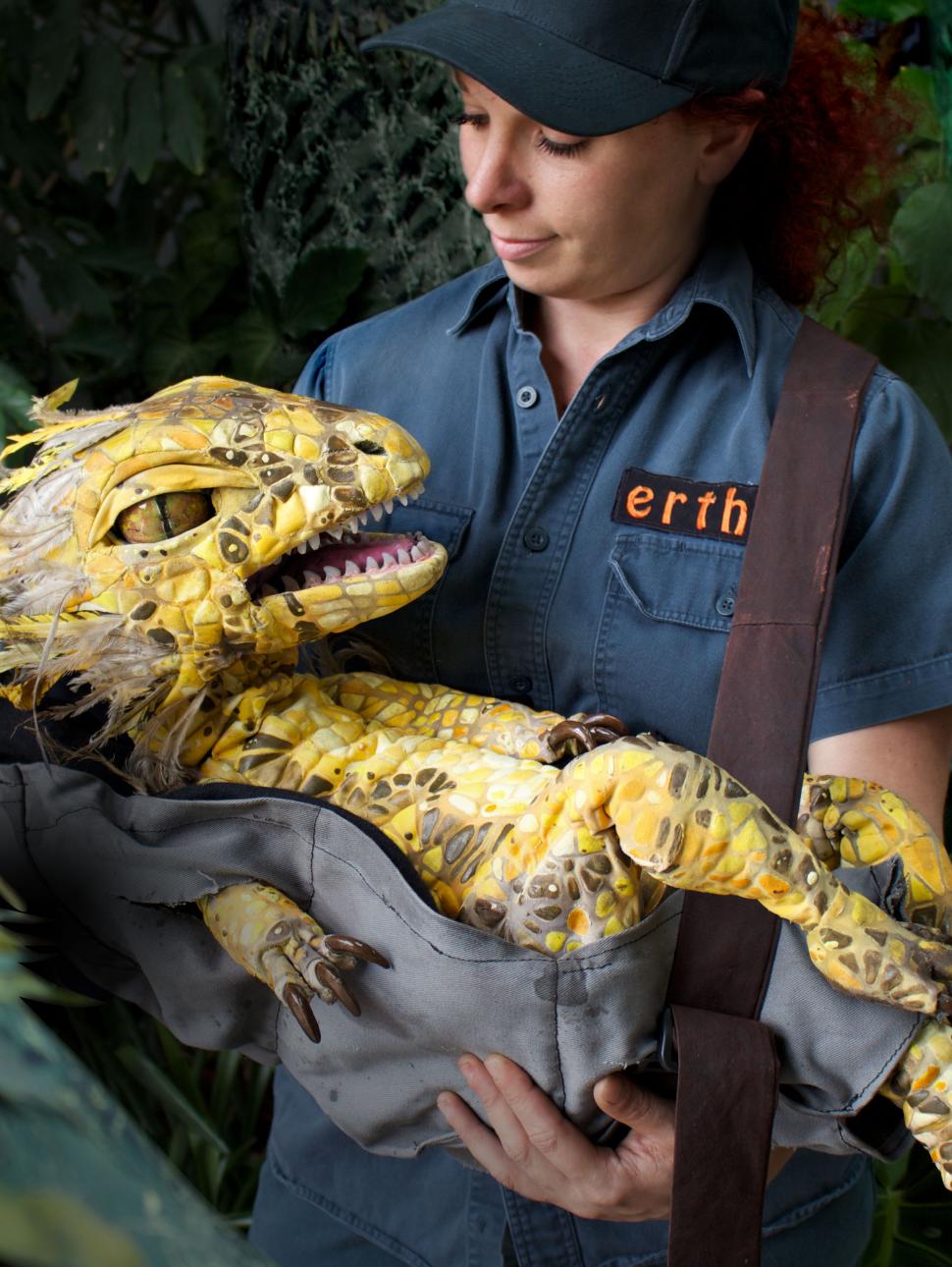 A young woman wearing an Erth's Dinosaur uniform holding a model baby dinosaur