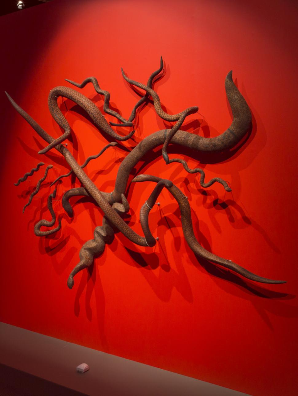 Snake sculptures from the Songlines exhibition are displayed against a vibrant red background