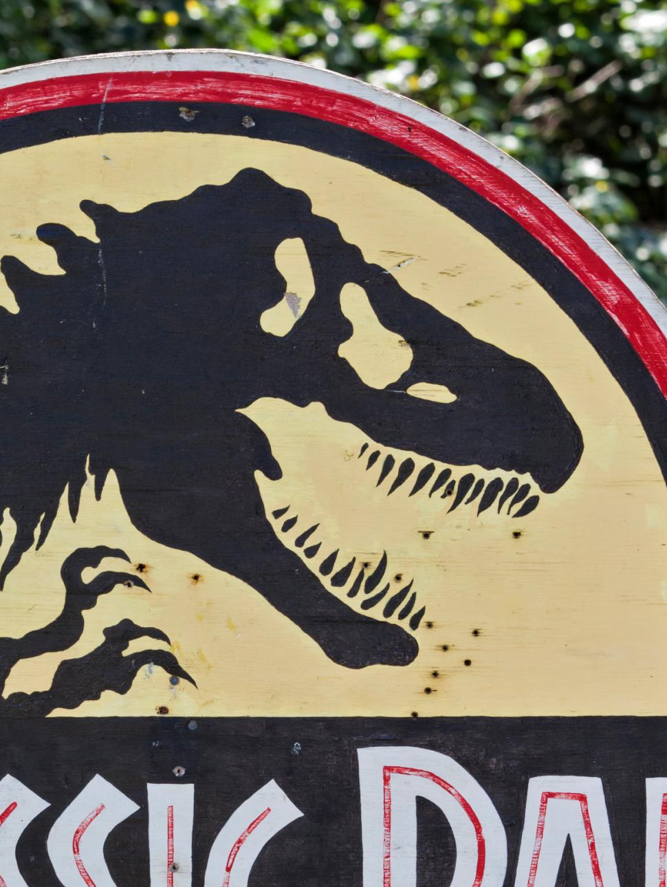 A Jurassic Park road sign in front of a green leafy background