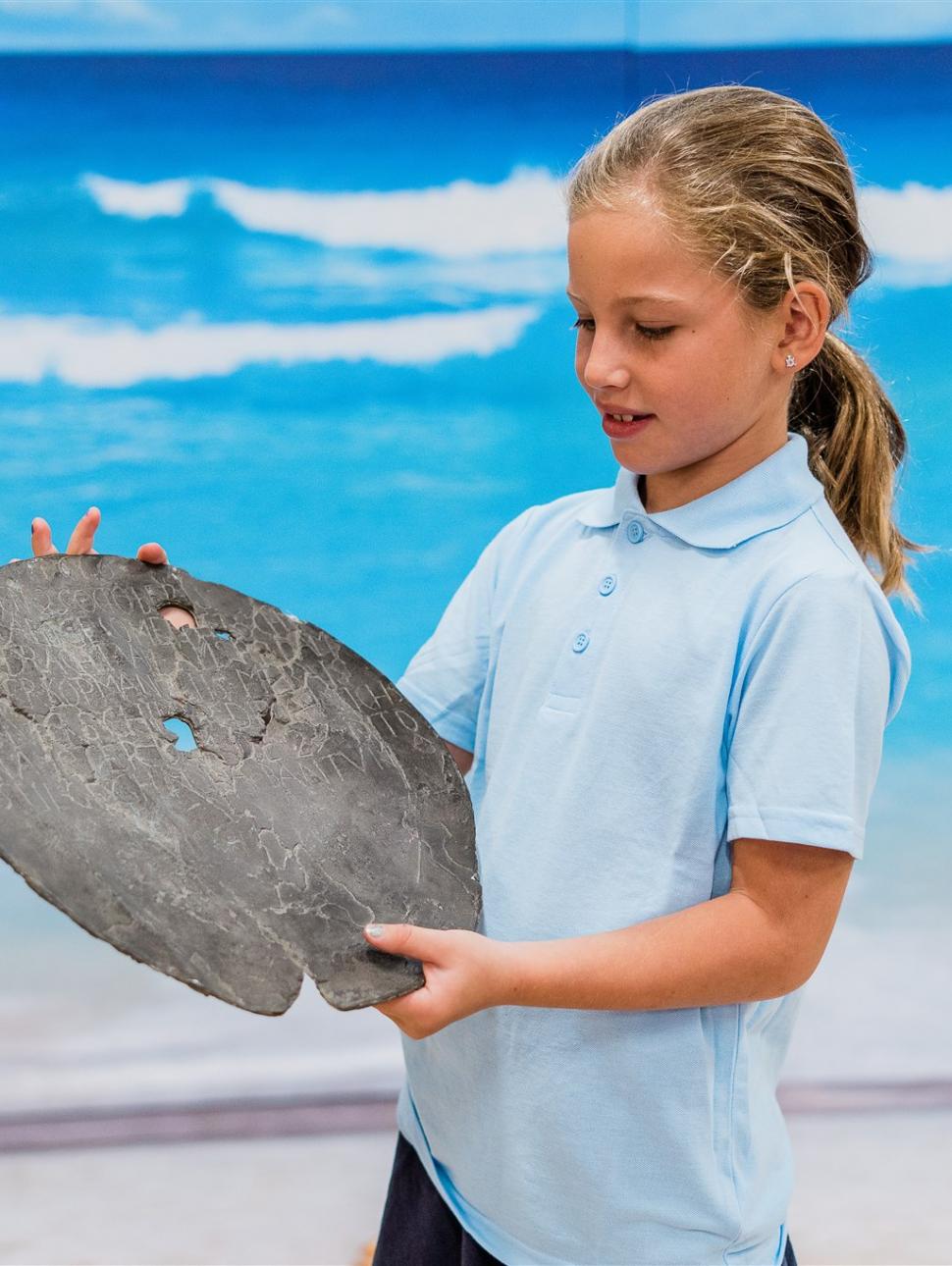 A blonde girl wearing school uniform examines de Vlamingh's plate