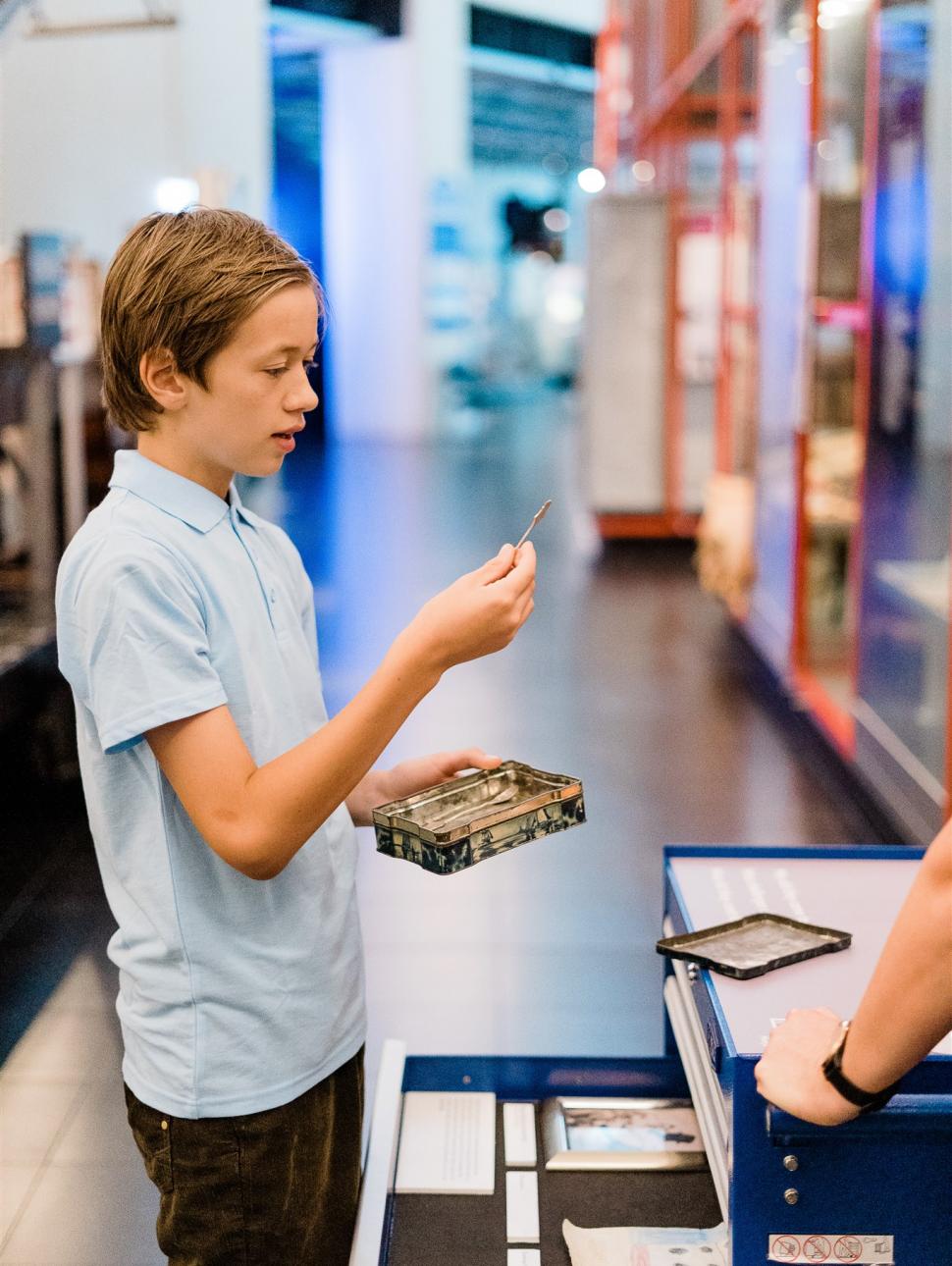 A boy looks intently at an object he has pulled from an old metal tin