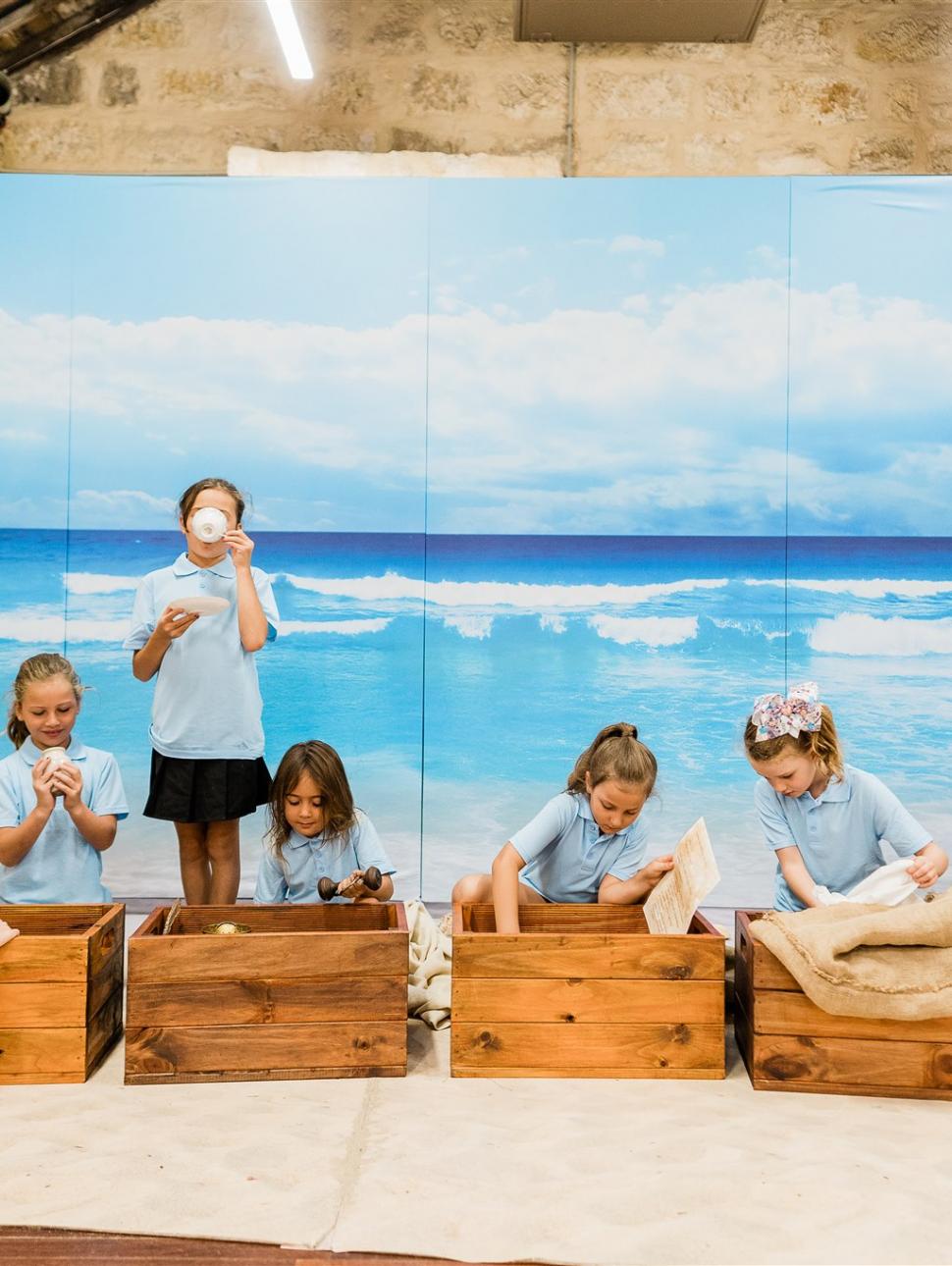 Girls in school uniform are unpacking a set of wooden crates in front of a painted backdrop