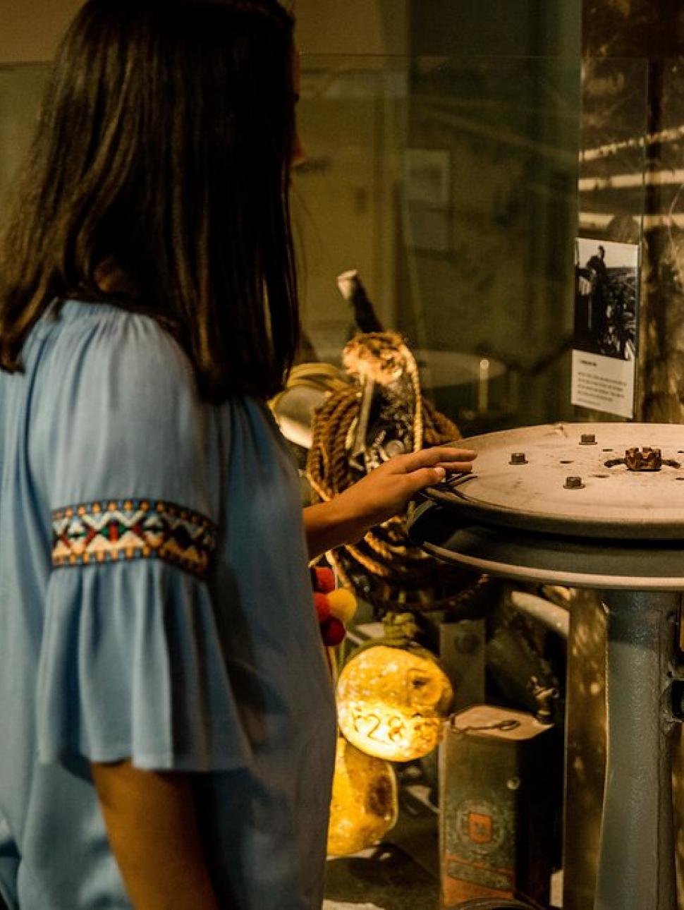 A person stands in a Museum gallery, touching an interactive exhibit