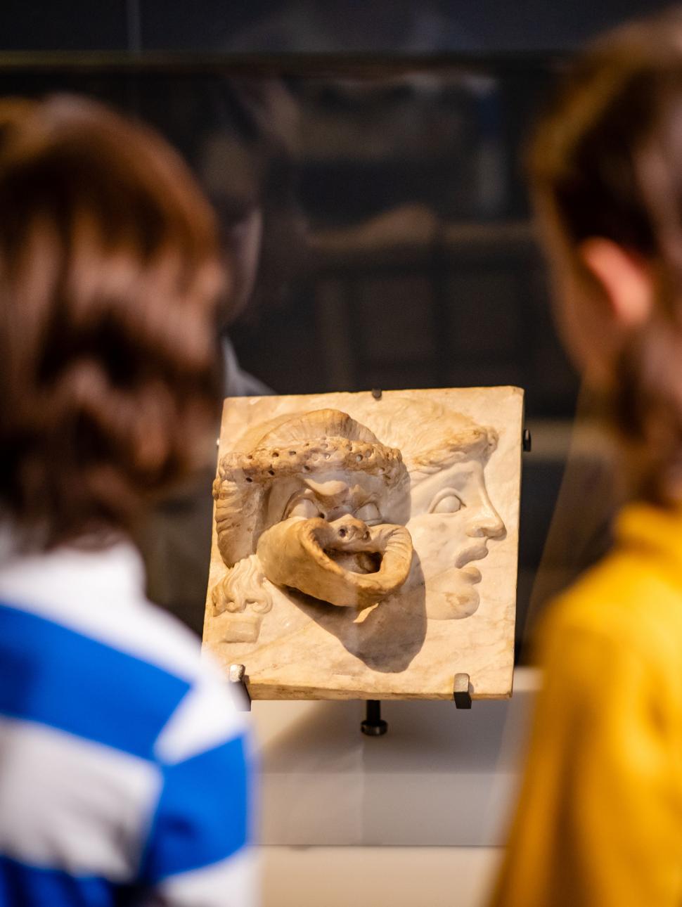 Two children looking at a sculpture of Ancient Greek Masks