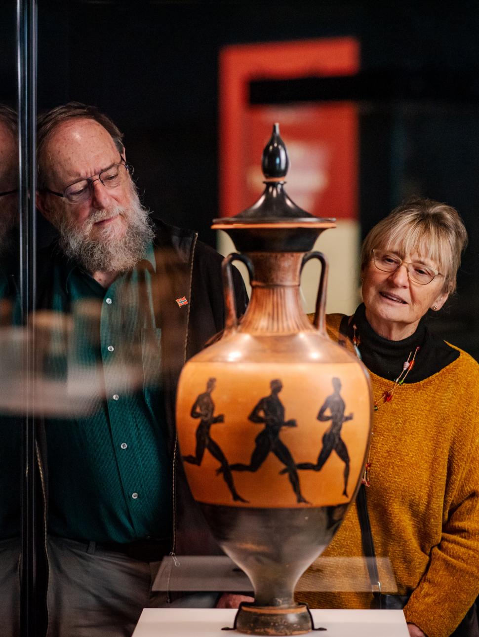 Two visitors admiring a vase with athletes depicted on it