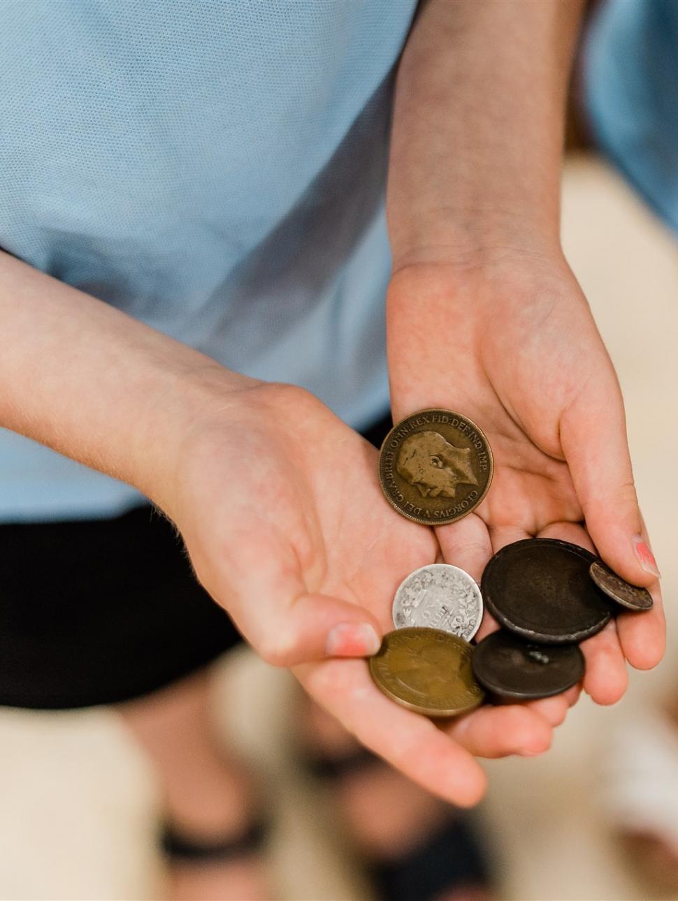 A close-up view of two children's hands holding old coins