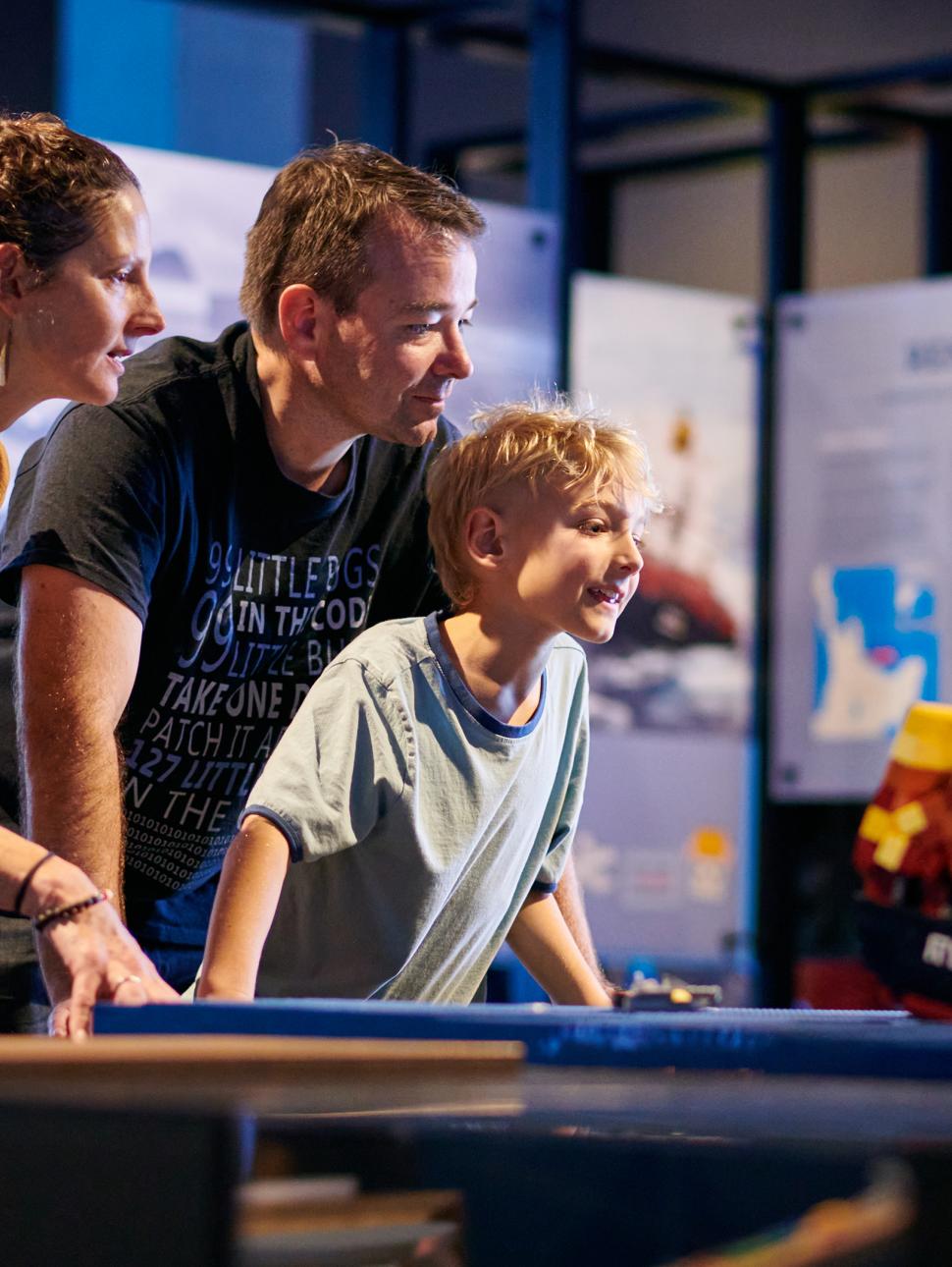 A young boy looks excitedly at a LEGO model of a ship with his family