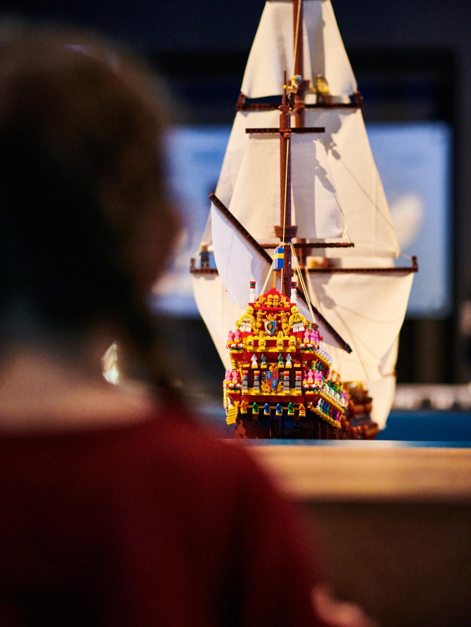 A young girl stands looking at an illuminated LEGO model of a ship in a museum display