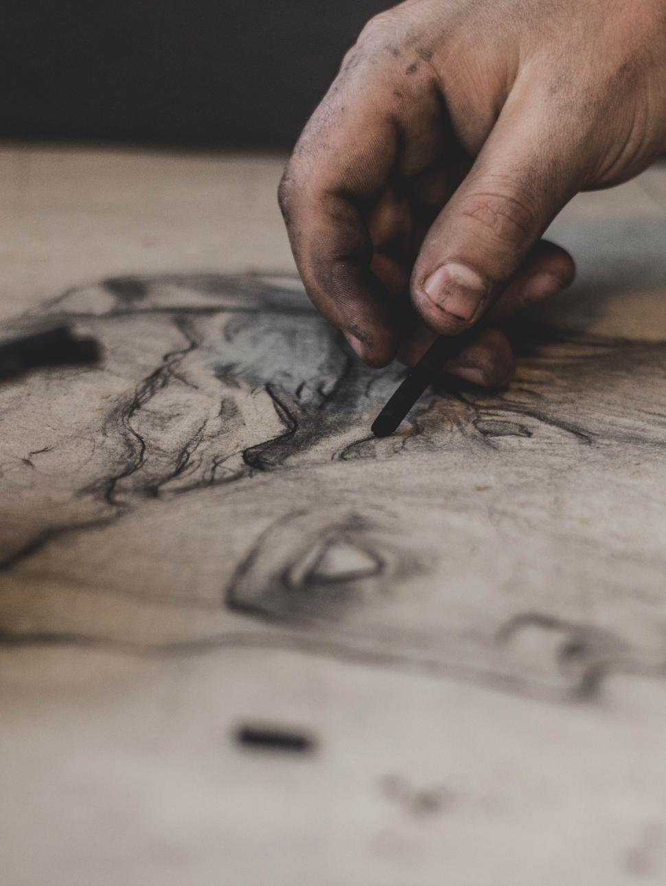 A close up of an artists hand drawing a sculpture head with charcoal