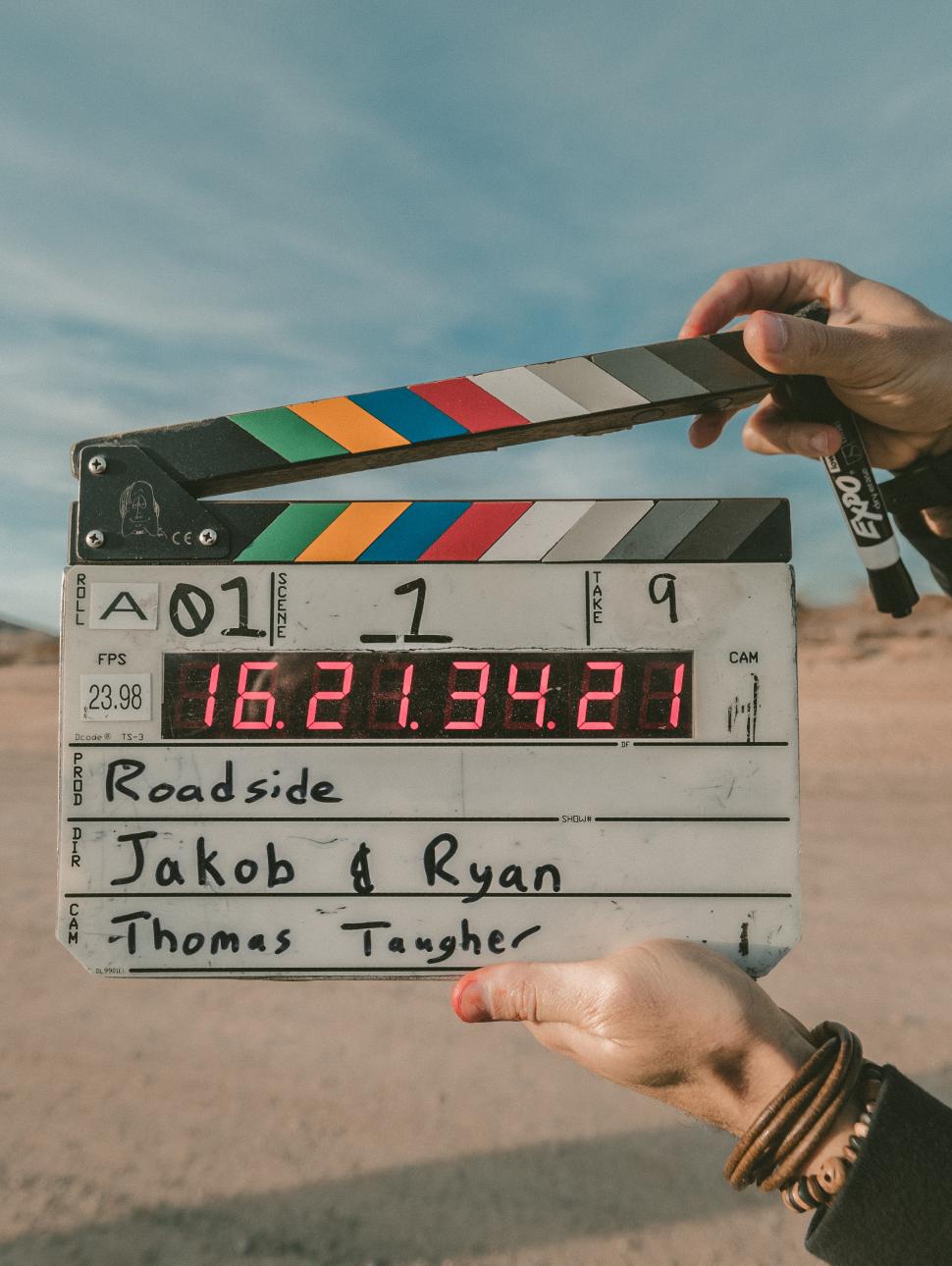 A film director holds a clapboard up in front of a desert landscape