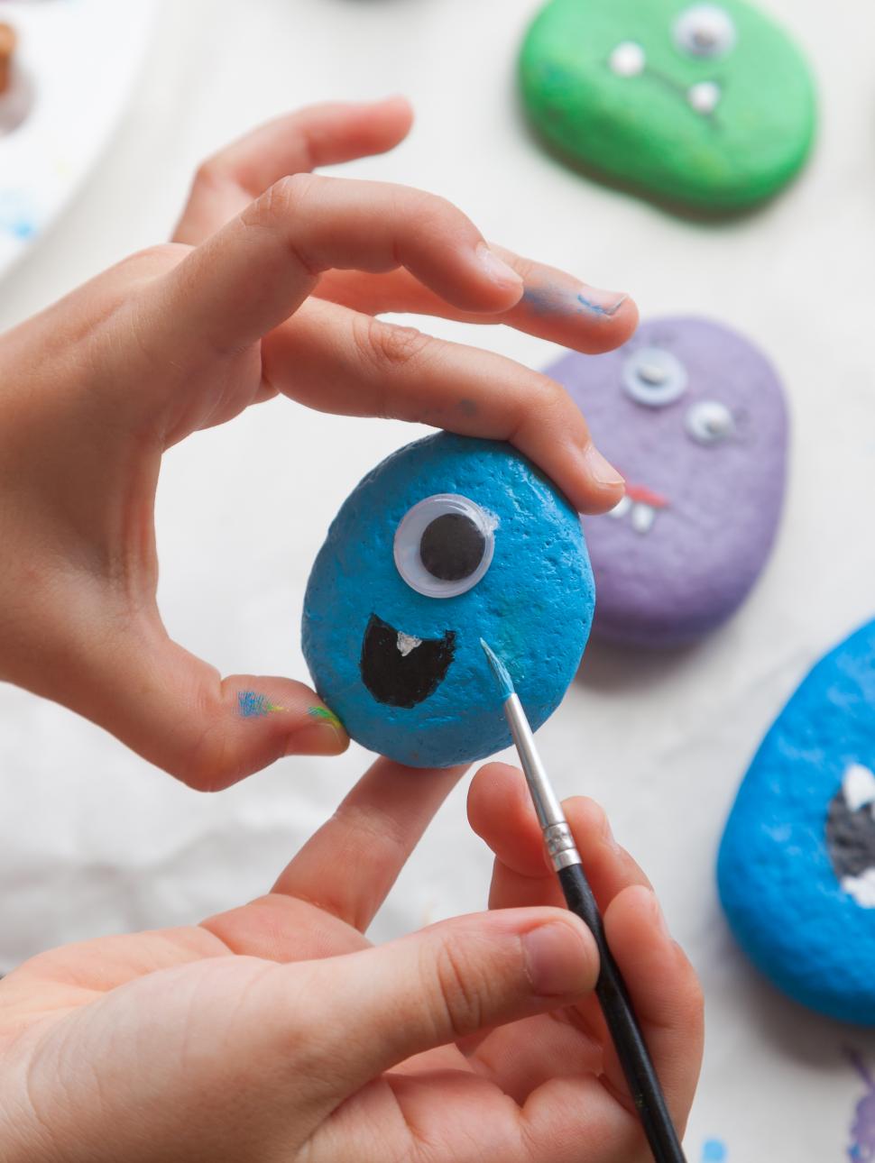 An image of hand painting a monster design on a rock.