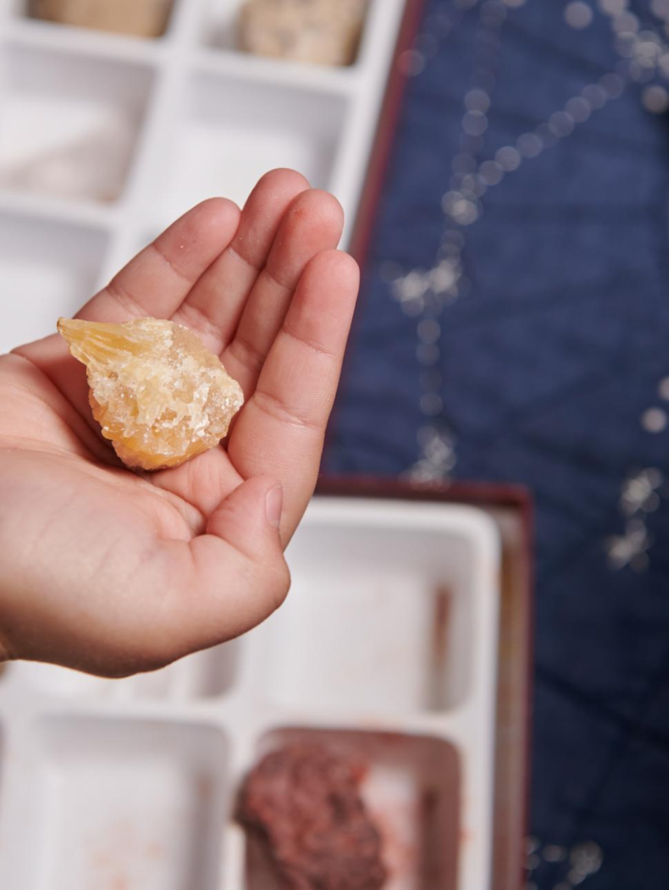 An image of a hand holding a rock with a series of rocks laid out behind 