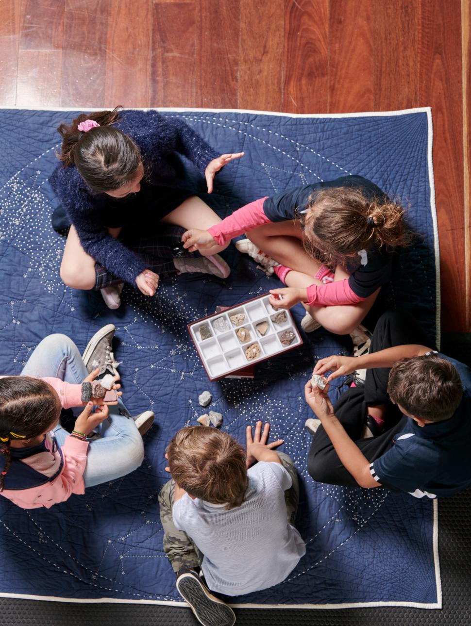 Five young people sitting together on a blue square mat, aerial shot