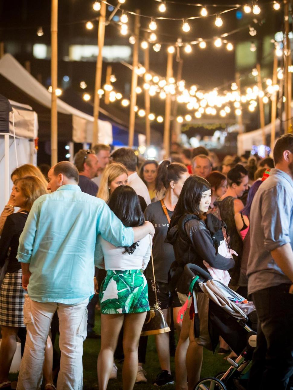 Fairy Lights and a crowd of people in colorful clothing at market stalls.