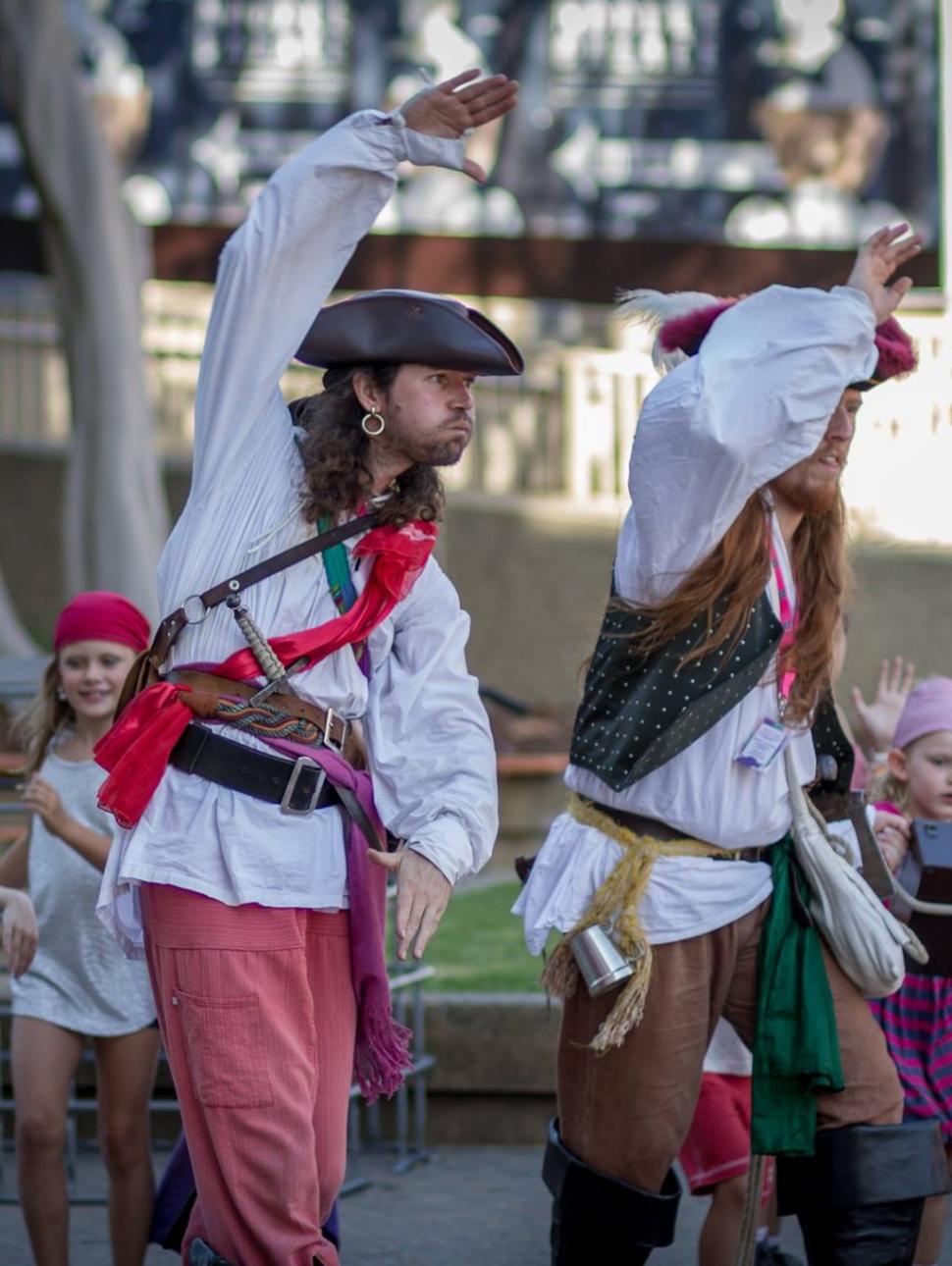 two pirates pretend they are swimming with a group of children dressed as crew members carrying treasure