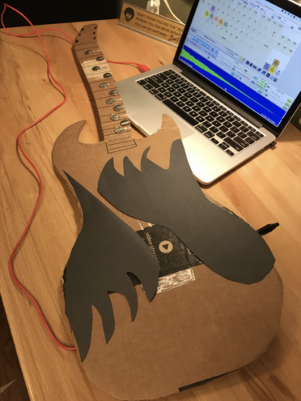 An image of a guitar made from recycled materials connected to a laptop coding program