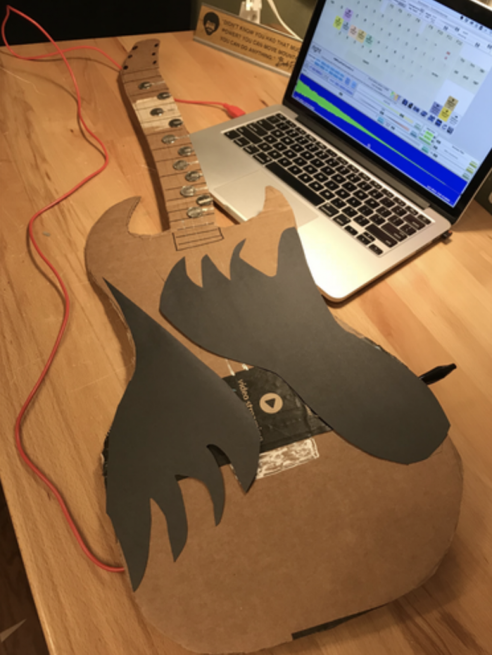 An image of a guitar made from recycled materials connected to a laptop coding program 