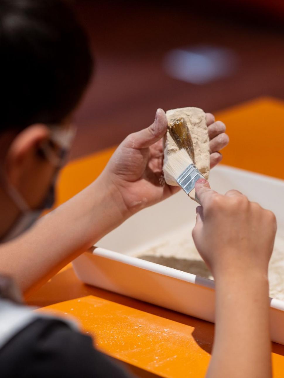 An image of a child carefully brushing sand from an object.