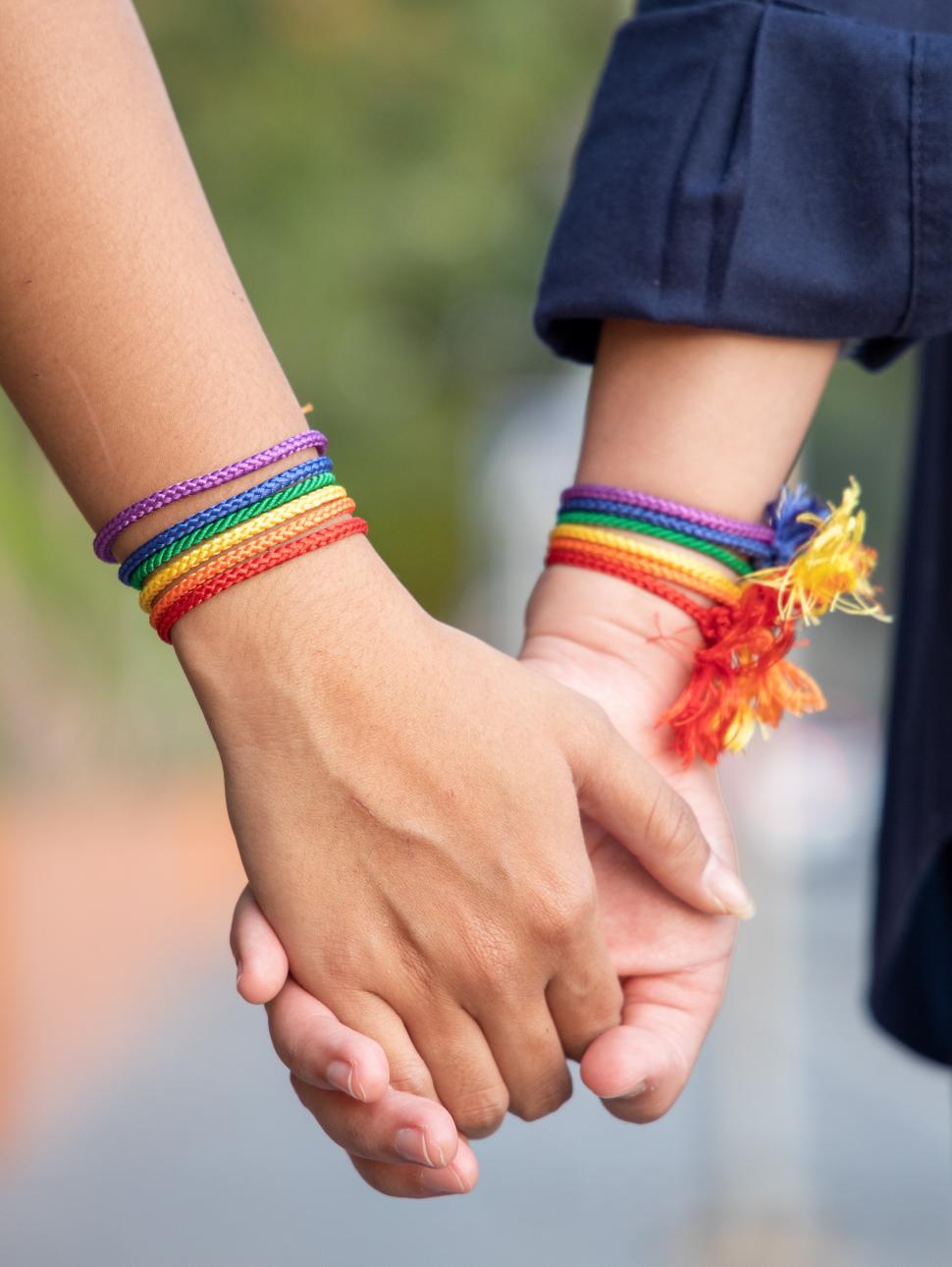 Two people holding hands with rainbow LGBTQI bracelets