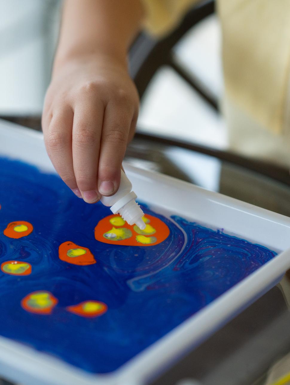 Small child places colour droplets on blue surface for marble painting
