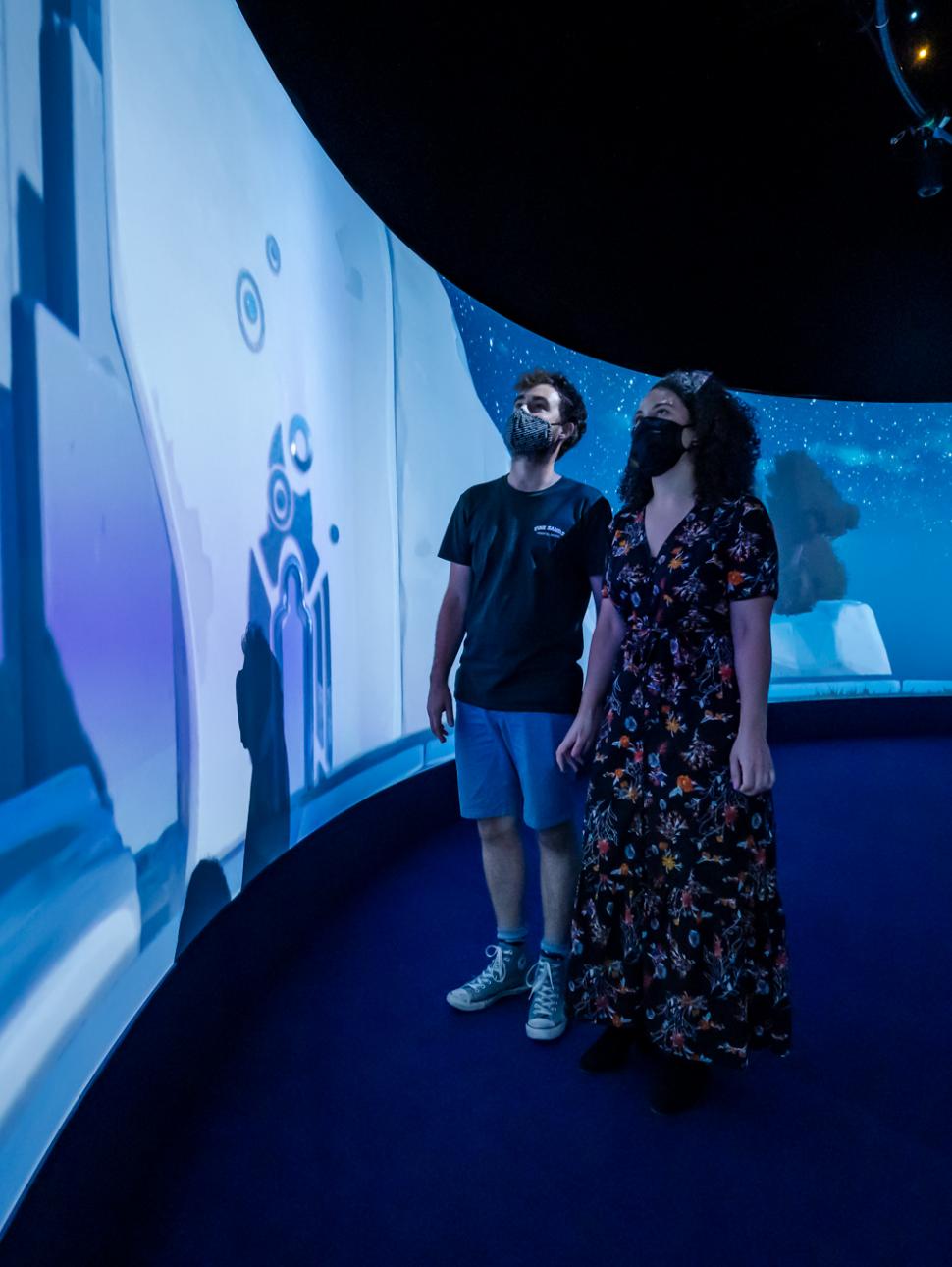 Two people look left to a digital wall, bathed in blue light