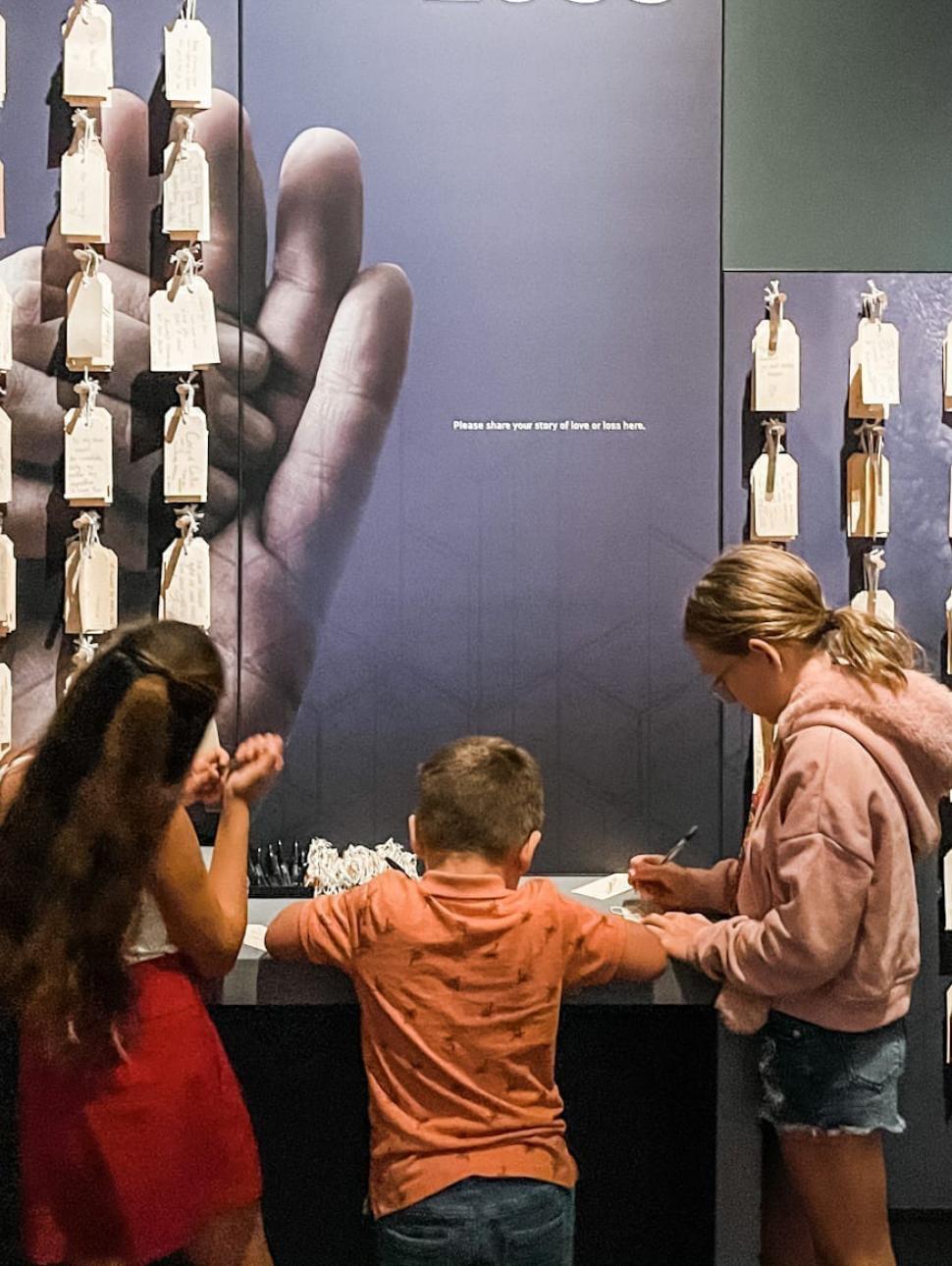 Three young people write notes in front of a wall of hanging notes