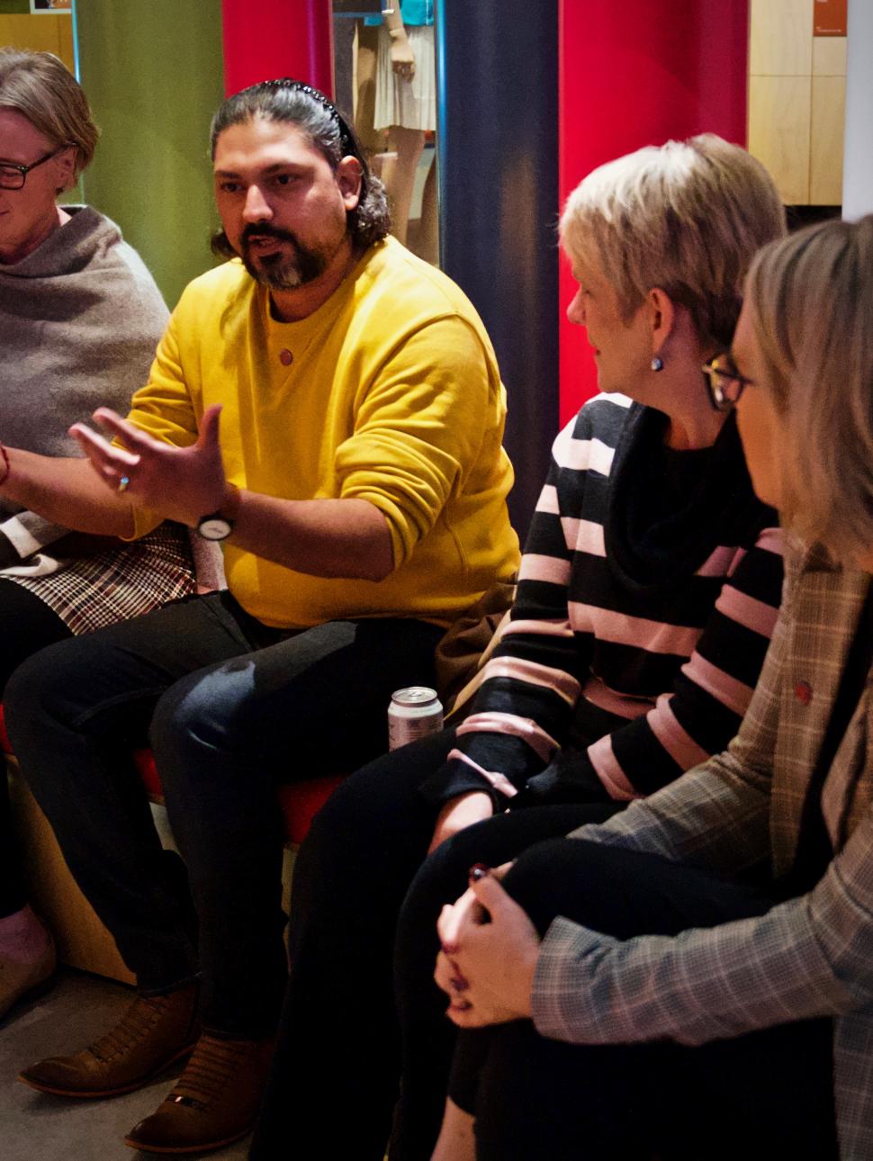 Four adults sit together in a line with one person speaking and the others looking on intently.