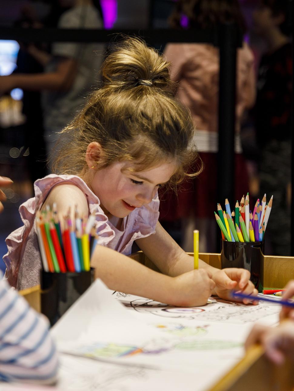 Girl with a high bun draws with coloured pencils at a small wooden table