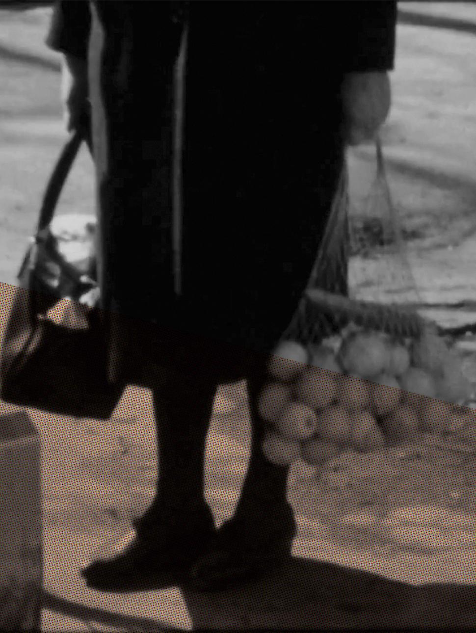 A black and white image of an older woman's knees, her hands holding a bag of oranges
