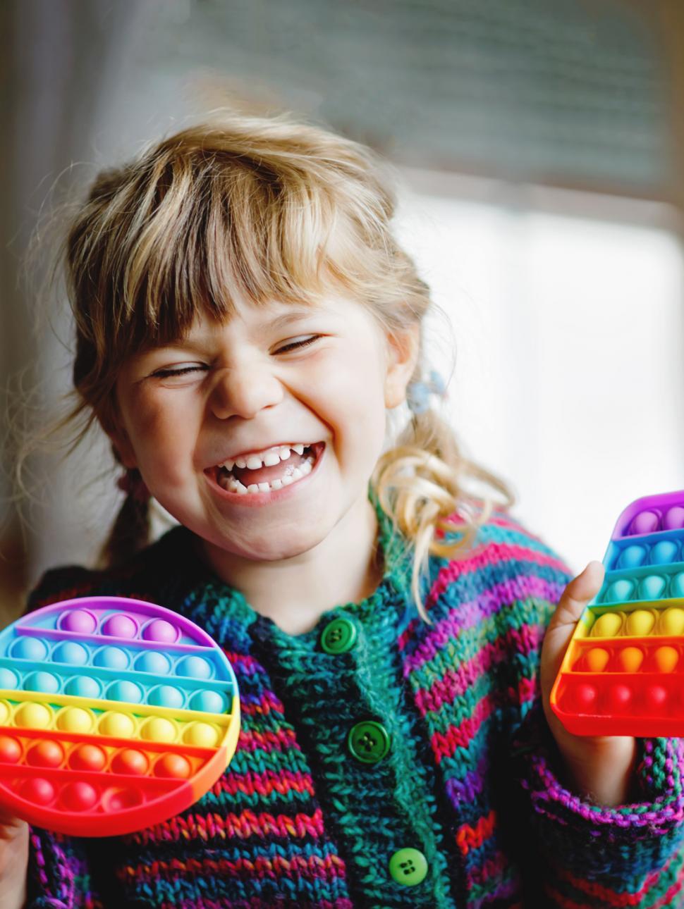 Little blonde preschool girl playing with new trend sensory toy - rainbow pop it. Antistress toy for children and adult. Colorful toy simple dimple. Squishy soft bubble toys rainbow color. Happy child