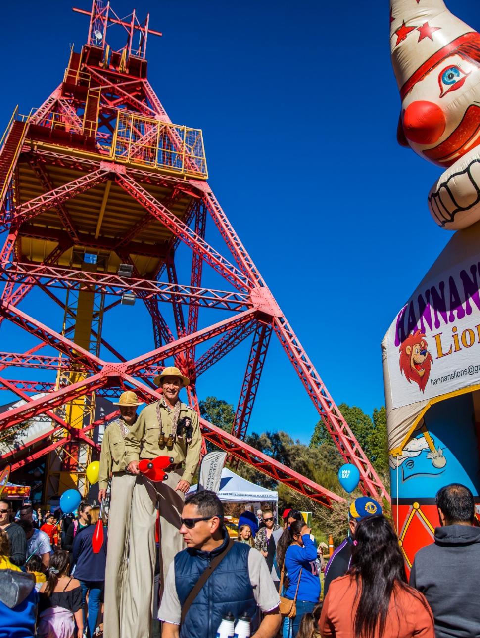 Image of a crown of people with stilt walkers and a bouncy castle