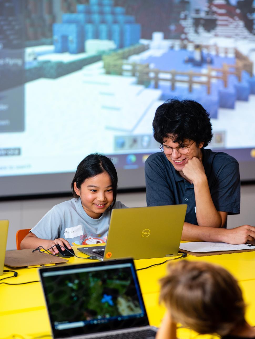 Two people looking at a laptop computer engaged in Minecraft design.