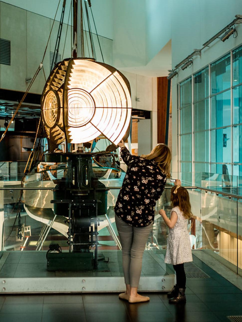 Mother and daughter look up at  a lighthouse replica on the second floor of WA Maritime Museum