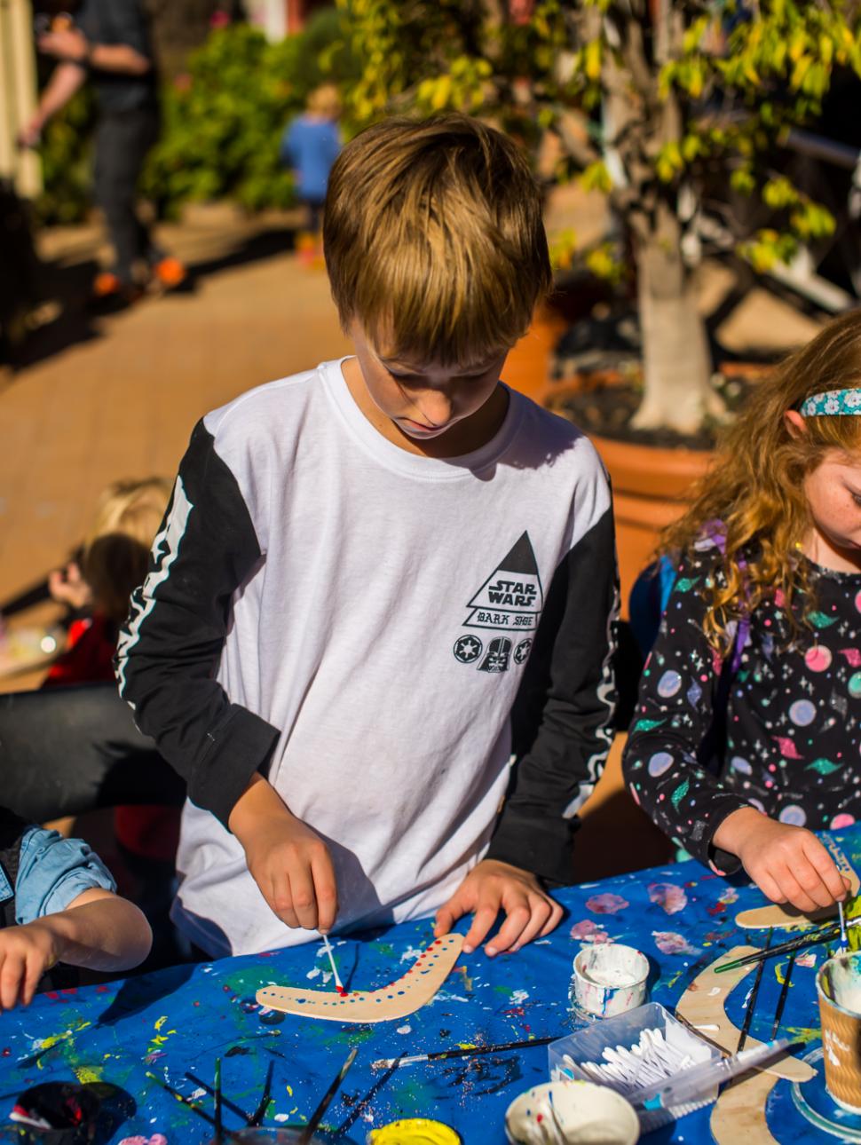 Young boy work son his art while standing above a desk outdoors