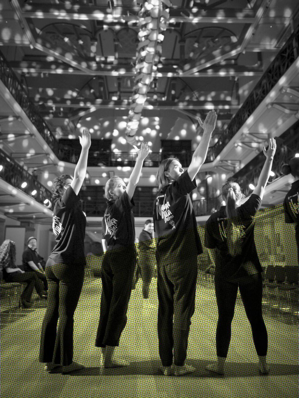 Four students stand under Otto the blue whale in Hackett Hall, gesturing up with their right arm