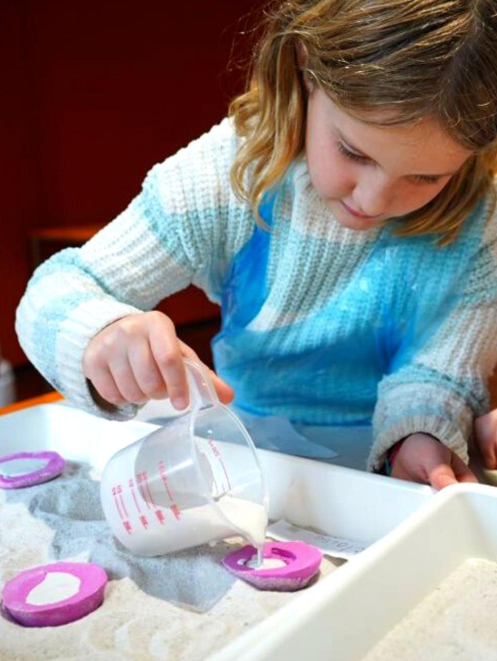 Image of a child in a school holiday program pouring plaster into a fossil cast