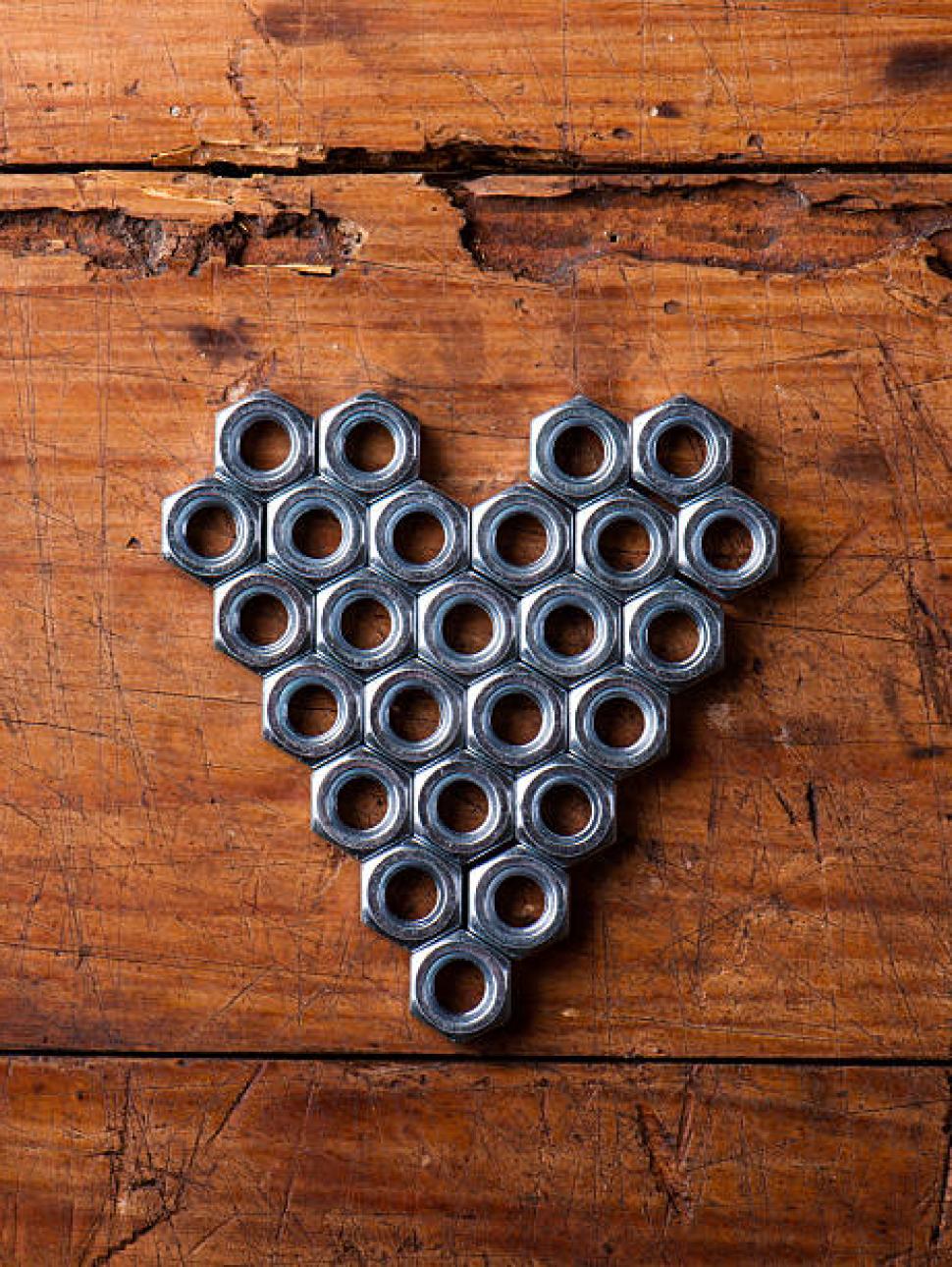 Metal nut bolts shaped in a heart positioned on a wooden board. 