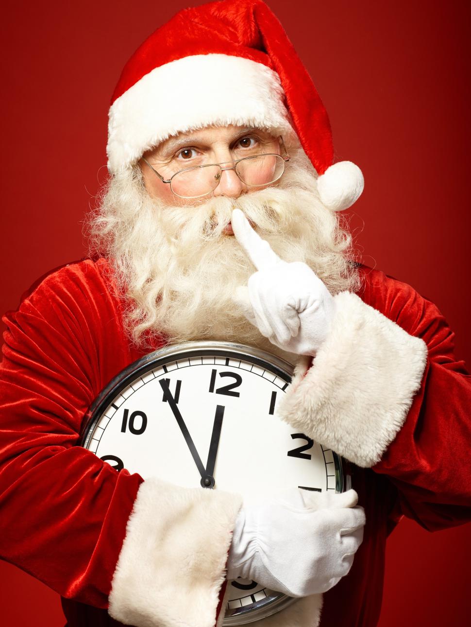 Image of Santa in a red velvet hat and suit holding a clock. 