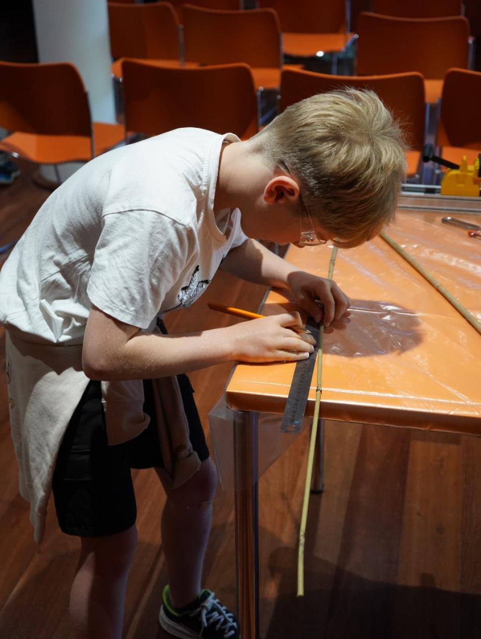 A boy using hand tools to cut bamboo to make a bee hotel