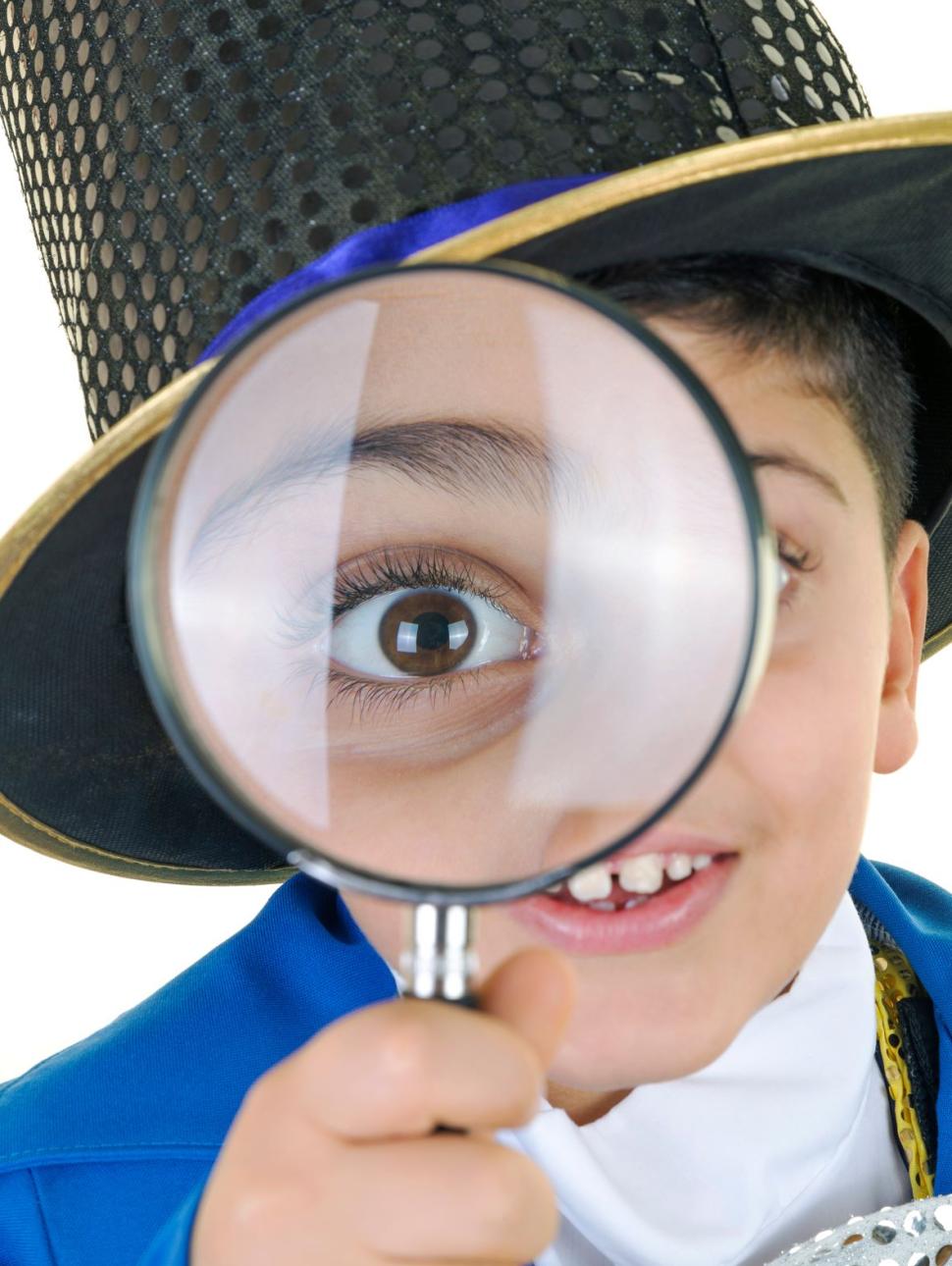 Child dressed up as Mad Hatter holds magnifying glass to face