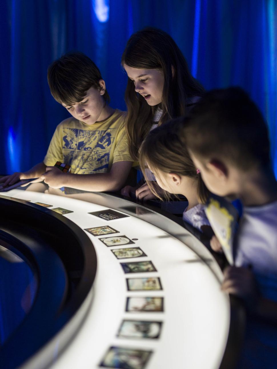 A group of children stare at a curved table top covered in photos