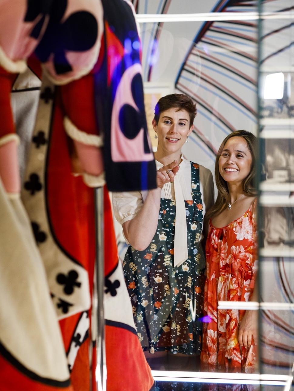 Two persons look through the protective museum glass at a large and colourful costume 